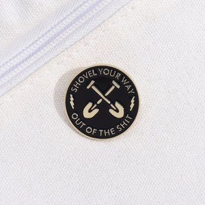 Detail of round black enamel brooch with Shovel Your Way Out Of The Shit metal slogan