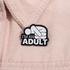 Gros plan d'un pin's émaillé I'M AN ADULT sur le revers d'un denim rose pastel