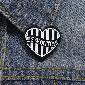 Cartoon heart enamel pin with black and white stripes and It's Showtime text on denim