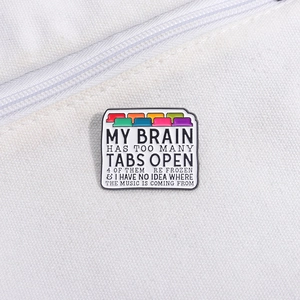 Macro detail of enamel pin showing colorful browser tabs and creative humor text on fabric