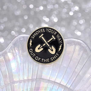 Round black enamel brooch with golden crossed shovels and motivational typography
