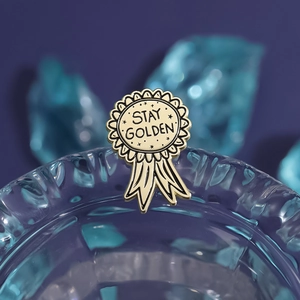 Spilla rotonda dorata con slogan Stay Golden e dettagli di stelle su fondo scuro