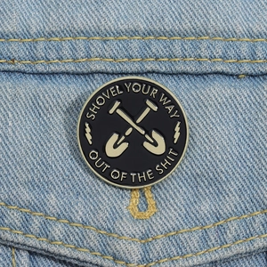 Macro view of a round enamel shovel pin with gold slogan on blue denim fabric