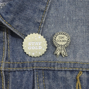 Set di due spille dorate con testo Stay Gold appuntate sul colletto di jeans