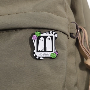 Detail of ghost enamel pin with roses and 'NO FEET' text on a green canvas bag