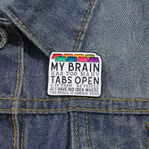 Colorful My Brain Has Too Many Tabs Open enamel pin on a dark blue denim jacket collar