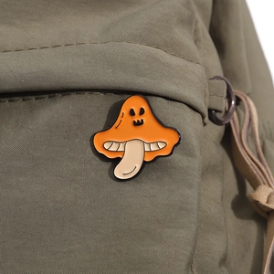 Nahaufnahme einer süßen orangefarbenen Emaille-Pilznadel mit Halloween-Gesicht auf der Tasche