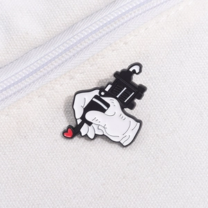 Detail of hand holding a tattoo machine enamel pin with red heart on white canvas