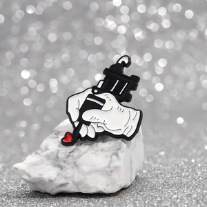 Artistic tattoo machine hand enamel pin with heart detail on a white stone background