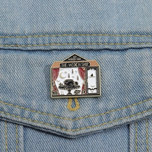 Detail einer Emaille-Anstecknadel mit 'The Witch Shop' Motiv auf blauem Denim-Hintergrund