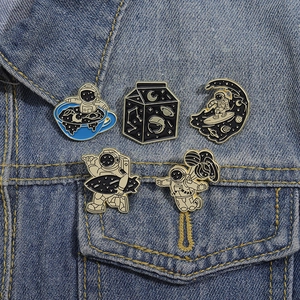 Five assorted cartoon astronaut enamel pins displayed on a denim jacket pocket