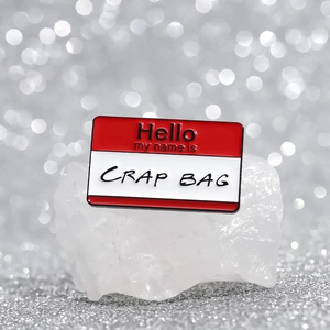 Funny enamel pin featuring 'Hello my name is CRAP BAG' text on a red and white name tag