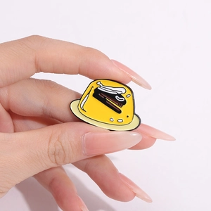 Close-up of hand holding a funny yellow pudding enamel pin with a stapler design