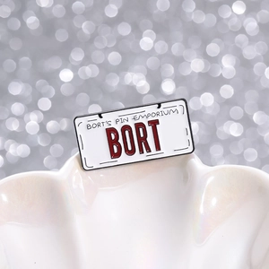 Retro BORT license plate enamel pin displayed on a pearl shell with bokeh background