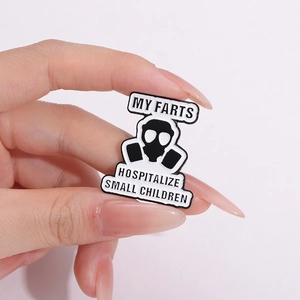 Macro detail of enamel pin with gas mask icon and funny text held by hand