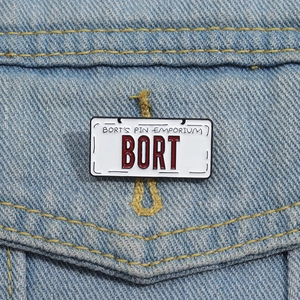 Macro shot of BORT license plate enamel pin on a denim jacket pocket edge