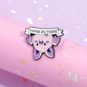 Cute enamel bat pin with 'Hang In There' text on soft pink and purple pastel background
