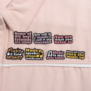 Close-up of music-themed enamel pins with English quotes on pink denim jacket pocket