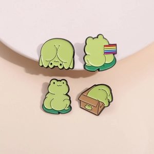 Four unique cartoon green frog enamel pins displayed on a minimalist beige background