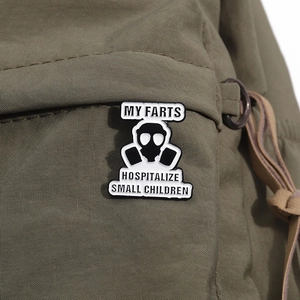 Funny gas mask enamel pin with humorous text on olive green canvas bag accessory
