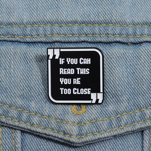 Detail einer Emaille-Anstecknadel mit Spruch auf Jeansstoff in Schwarz und Weiß