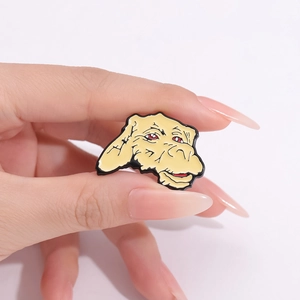 Macro view of a cartoon yellow alien enamel pin held by a hand showing compact size