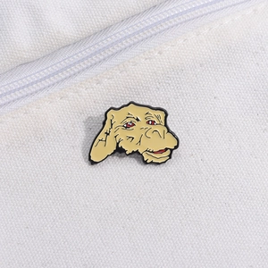 Macro detail of khaki alien enamel pin with red eyes on white canvas backpack surface