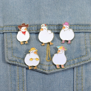 Set of five cute white enamel goose pins with various hats on blue denim background