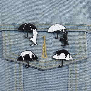 Set of four cartoon cat and umbrella enamel pins displayed on a blue denim jacket pocket