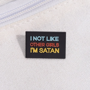 Macro detail of black enamel Satan brooch with colorful text on white canvas background