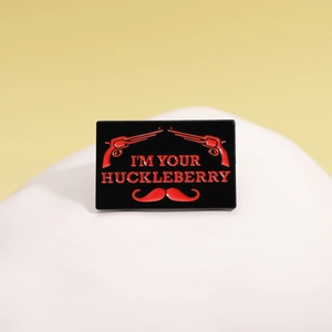 Black rectangle enamel pin featuring red revolvers, mustache, and I'M YOUR HUCKLEBERRY text