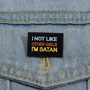 Detail of rectangular black enamel brooch pinned on a denim jacket featuring rebel text