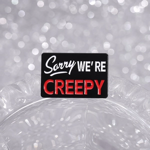 Rectangle enamel pin with black background and Sorry We Are Creepy text on glittery backdrop