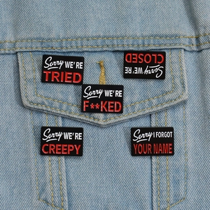 Macro shot of five black enamel pins with slogans on a blue denim jacket pocket