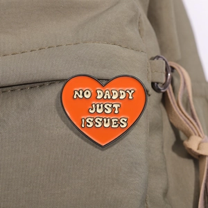 Détail d'un pin's coeur orange émaillé avec texte sur la sangle d'un sac à dos en toile