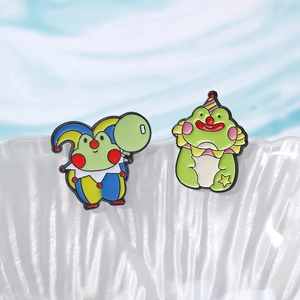 Detail of two cartoon frog enamel pins with circus clown outfits on a ceramic edge