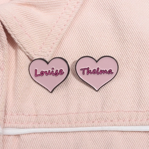 Détail de pins cœur en émail rose avec écritures Louise et Thelma sur veste en jean