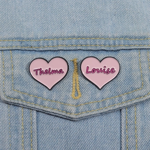 Close-up of pink heart enamel pins with Thelma and Louise text on a denim jacket
