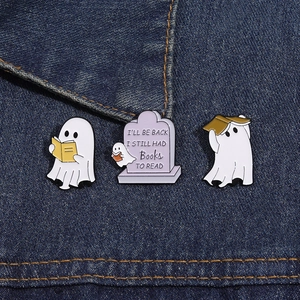 Three cute ghost reading enamel pins attached to deep blue denim fabric background