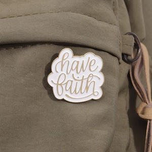 Close-up of cloud-shaped enamel pin with 'have faith' text on green canvas bag