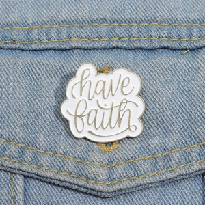 Detail of 'have faith' enamel badge pinned on blue denim pocket showing metal texture
