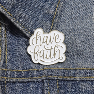 White enamel pin with golden 'have faith' text pinned on blue denim jacket collar