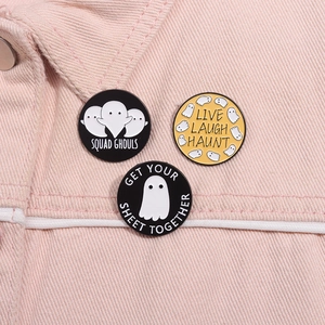 Detail of three Halloween ghost enamel pins pinned on pink denim fabric material