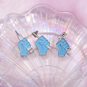 Set of 3 blue medical enamel pins with syringe and hammer shapes on pink fabric