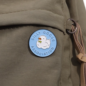 Detail of Silly Goose Association enamel pin on olive green canvas backpack fabric