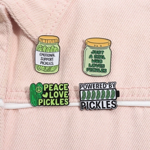 Close-up of four creative enamel pickle pins attached to pink denim fabric showing details