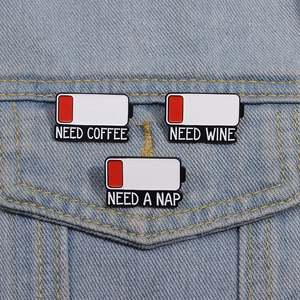 Detail of creative low battery enamel pins with Need Coffee, Wine, Nap text on denim