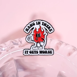 Funny cartoon red flame enamel pin with Hang In There text on a soft pink background