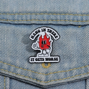 Detail of red flame enamel pin with Hang In There text on light blue denim jacket
