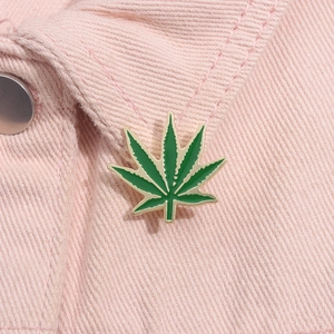 Detail of green leaf enamel brooch pinned on pink denim jacket showing metal texture